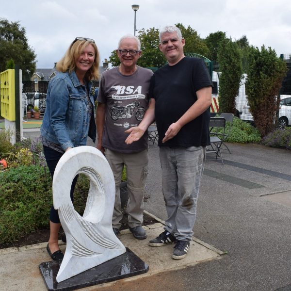 Three people gather around Tom Allan's sculpture 'Big Wave Vortex' which is installed in a small urban garden.