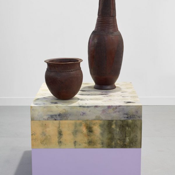 two brown clay vessels ontop of a tye-dyed fabric covered plinth. Yellow and lilac