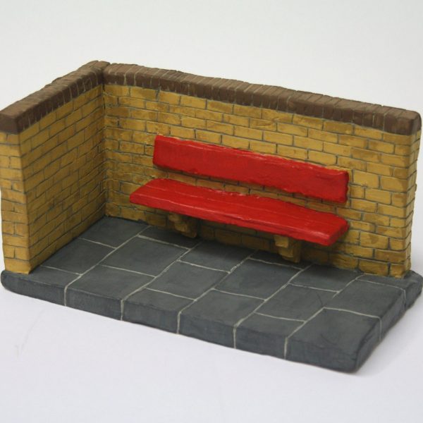 a small clay sculpture of a corner of wall and pavement with a red bench