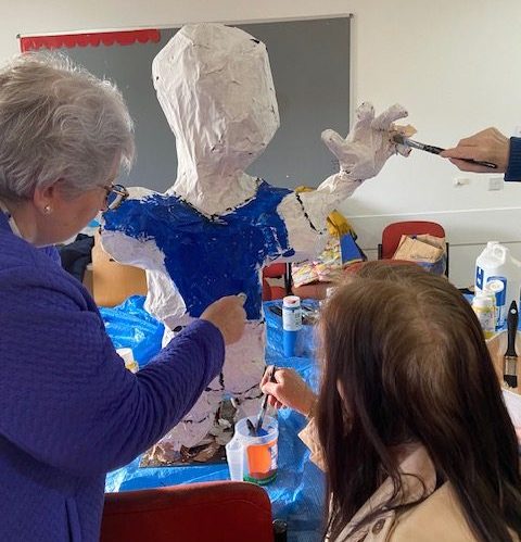 3 people paint a paper mache sculpture with a blue shirt